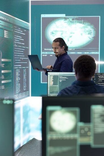 Professional hacker using ransomware and phishing tactics to compromise networks and gather intelligence for national security during cyberwarfare. Governmental spyware on big screen.